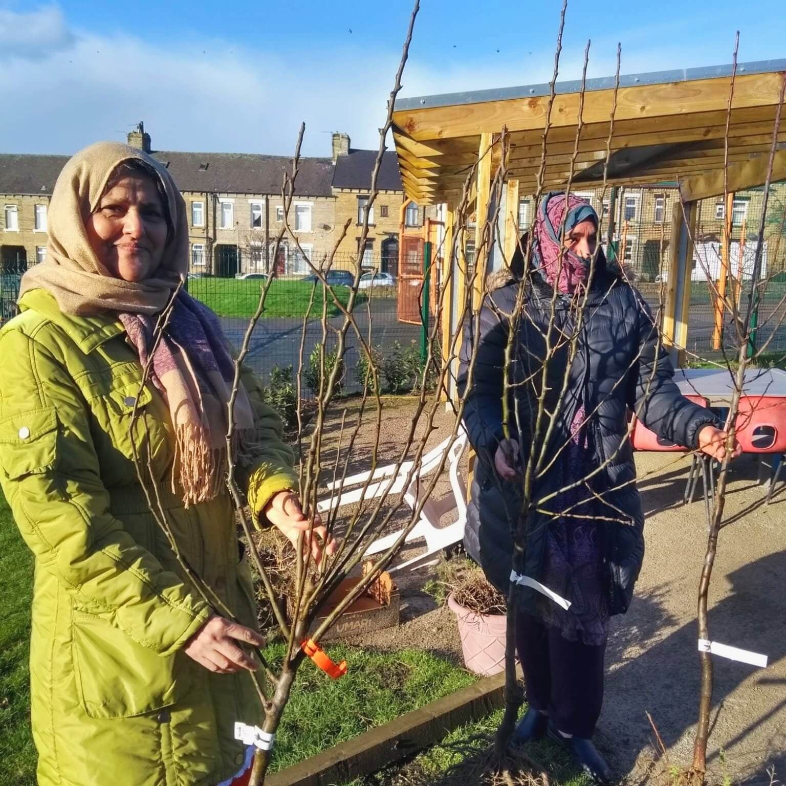 Two ladies, smiling and holding their sapling fruit trees